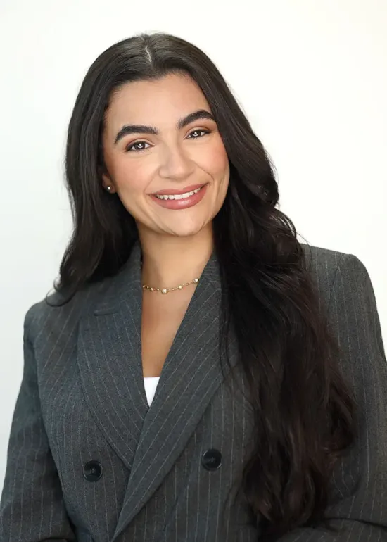 Woman with long dark hair in a gray pinstripe blazer, smiling at the camera against a light background.