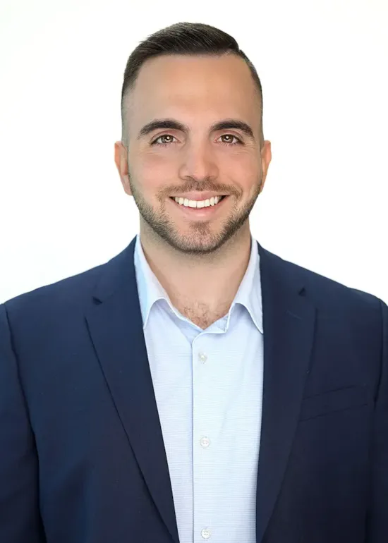 Smiling man in a blue suit jacket and light blue shirt, posing against a plain white background.