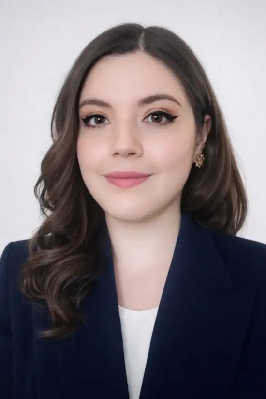 A woman with long brown hair in a navy blazer, white top, and gold earrings, smiling at the camera.