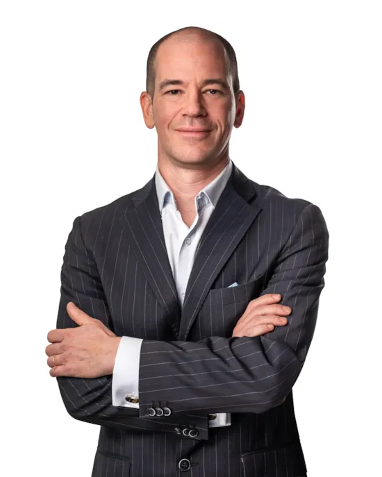 Man in a pinstripe suit with arms crossed, standing and smiling against a white background.