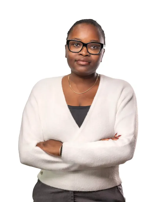 A woman with glasses and a white sweater stands with arms crossed, looking at the camera against a white background.