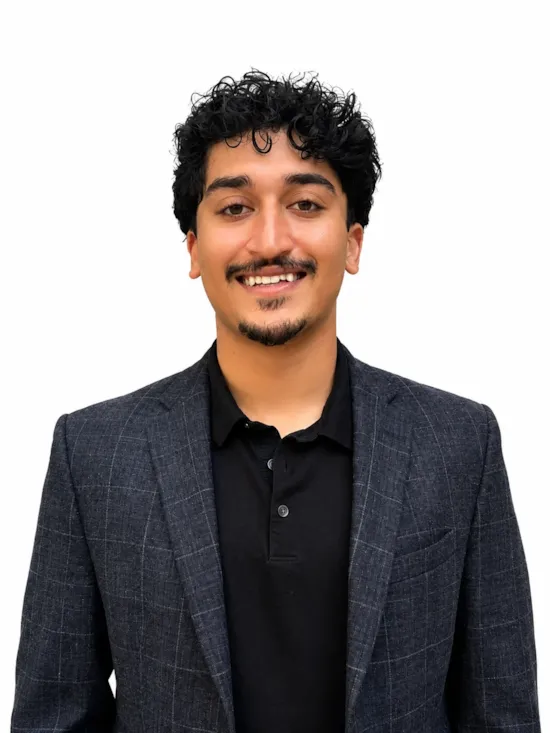 Professional headshot of a man with curly dark hair wearing a charcoal blazer and black polo shirt against a clean white background