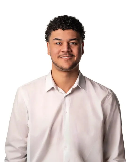 A young man with short curly hair smiles, wearing a white button-up shirt, standing against a white background.