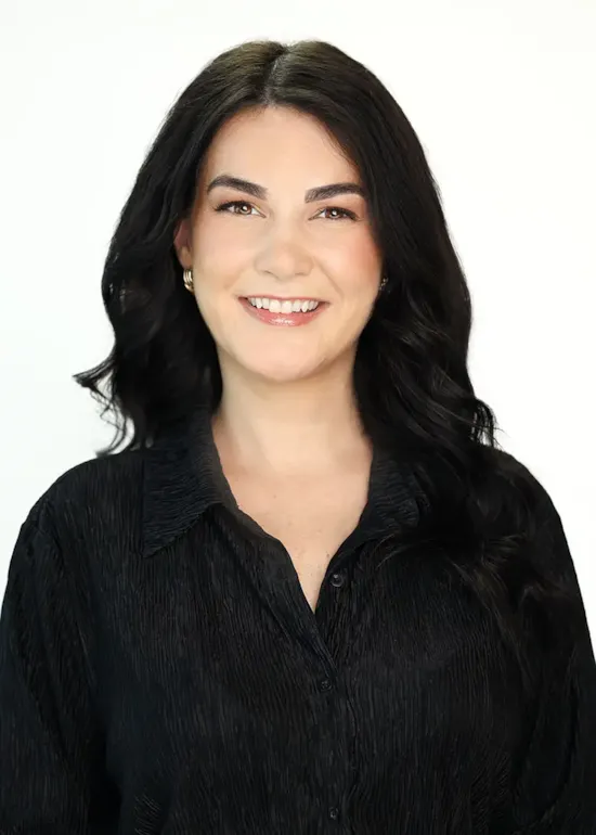 Smiling woman with long dark hair wearing a black shirt, posing in front of a plain white background.