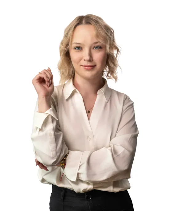 Woman with blonde hair in a white blouse stands confidently with arms crossed, smiling slightly, on a white background.