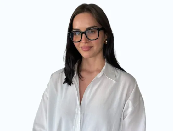 Woman with long brown hair and glasses, wearing a brown top, stands with arms crossed against a white background.