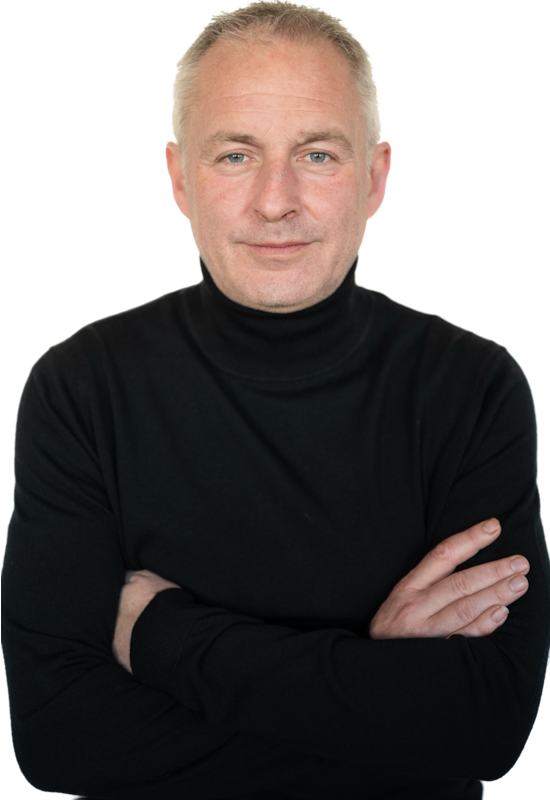 Man with short gray hair wearing a black turtleneck, arms crossed, standing against a plain white background.