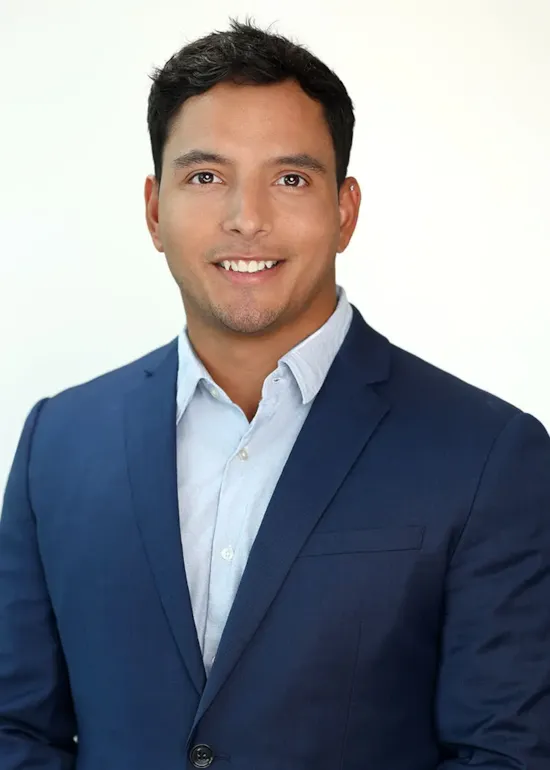 Man in a blue suit and light shirt smiling at the camera against a plain white background.