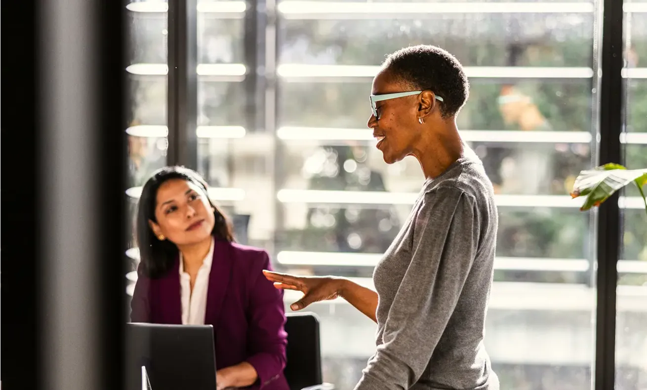 A woman speaking to engaged colleagues in an office conference room.