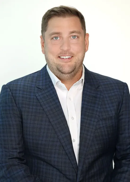 Man with short light brown hair wearing a blue plaid suit jacket and white shirt, smiling at the camera.