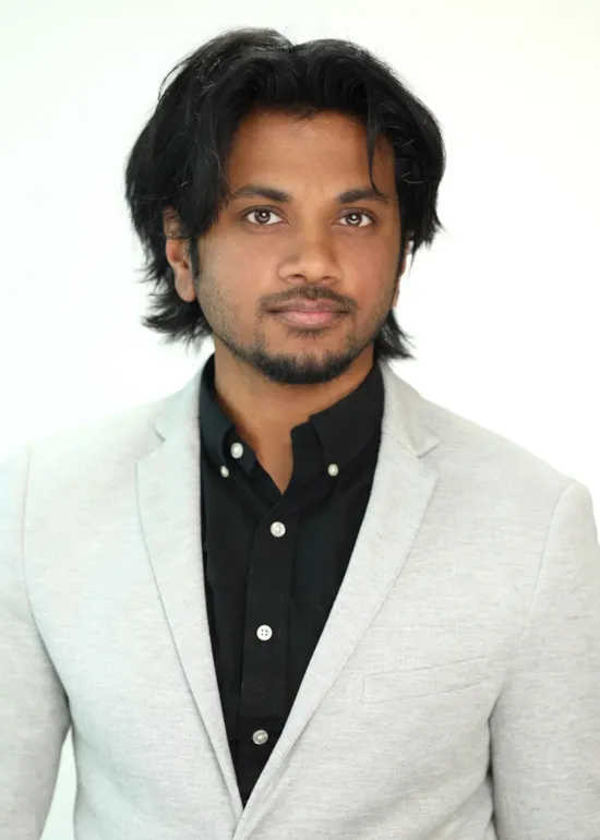 Man with medium-length dark hair and a trimmed beard wearing a gray blazer and black shirt, facing the camera.