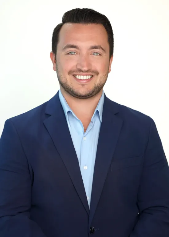 Smiling man in a blue blazer and light blue shirt posing in front of a plain white background.