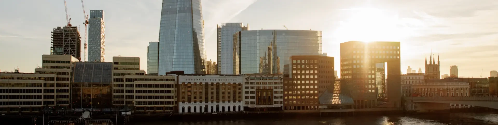 Modern office buildings and skyscrapers along the riverbank at sunset, with sunlight reflecting off the glass windows.