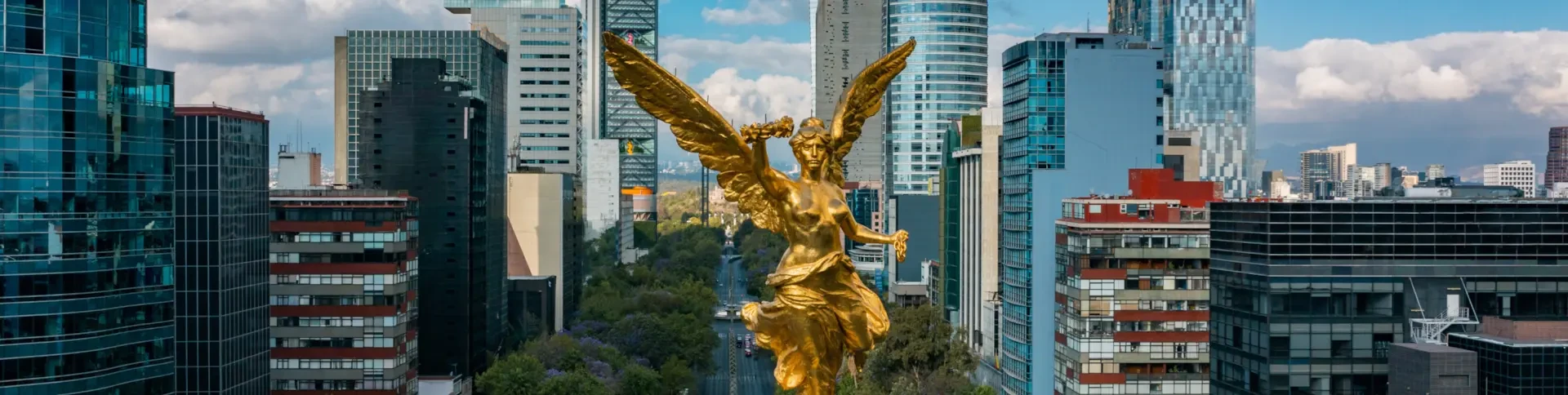 A golden angel statue stands amid tall modern buildings along a wide avenue in a cityscape under a partly cloudy sky.