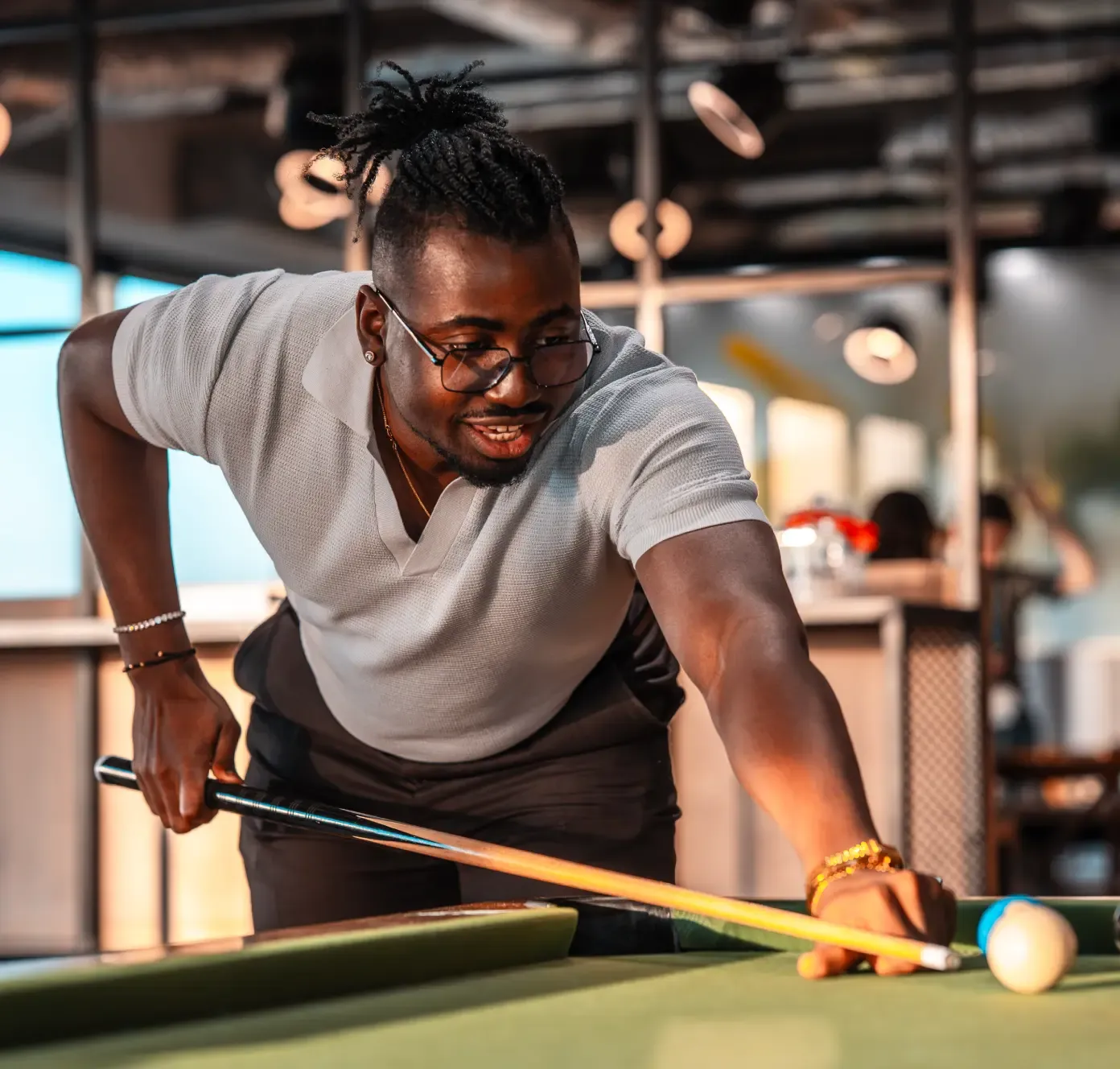A man in glasses aims a pool cue while playing billiards indoors, smiling and focused on his shot.