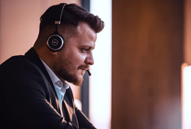 Man in a suit wearing a headset with microphone, looking at a screen, likely working or on a call.