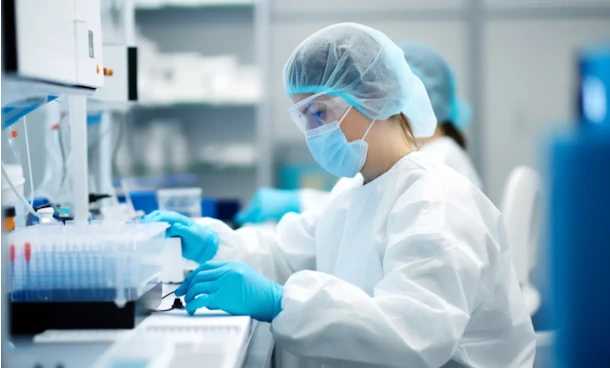 Lab technician in protective gear including hairnet, mask, and gloves working with samples in a laboratory.